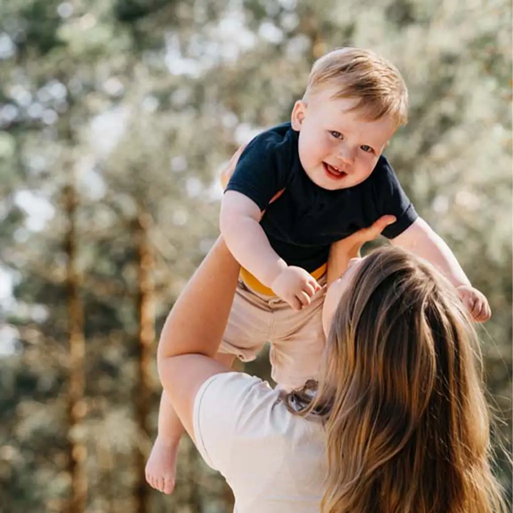 Moeder tilt haar kind op terwijl hij lachend in de camera kijkt tijdens de familieshoot op het Wekeromse Zand.