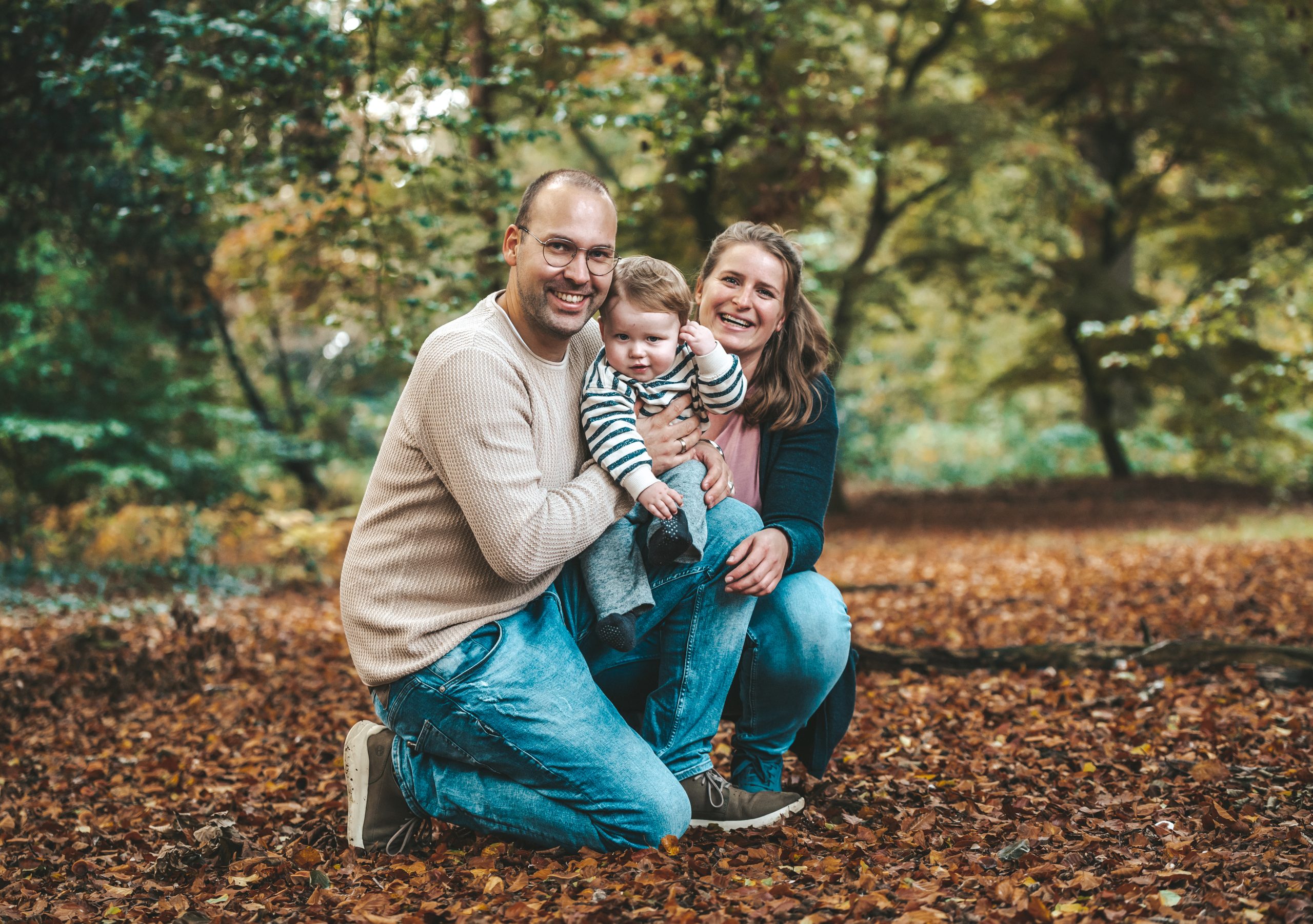 Kind zit op schoot van vader, moeder is gehurkt en zit liefdevol achter het kind en de vader tijdens de familieshoot